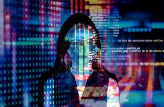 Illustration d'une femme face à l'écran avec du code informatique en arrière-plan, pour l'article sur l'intelligence artificielle dans la formation, avec des couleurs se reflétant sur elle pour représenter l'intégration de la technologie.